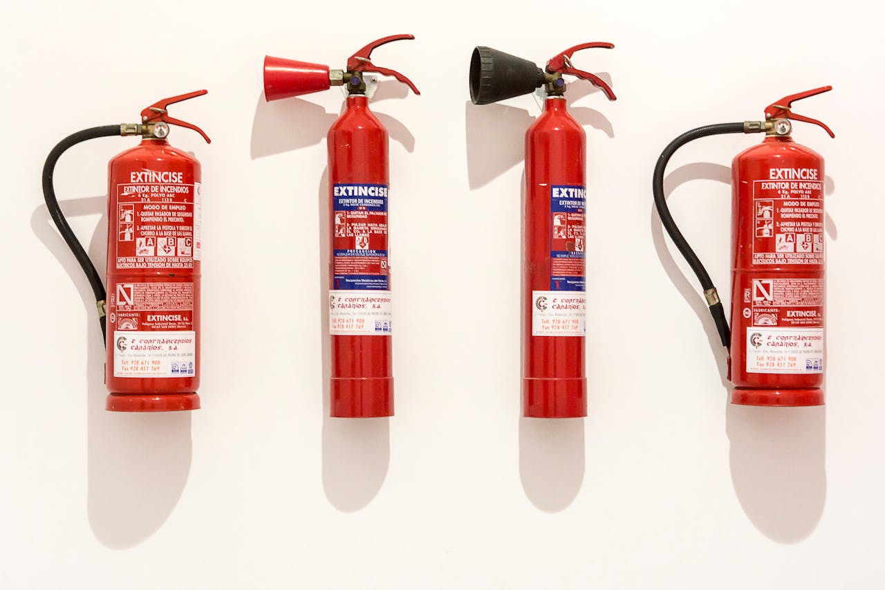 Four red fire extinguishers hanging on a clean white wall in an orderly fashion.
