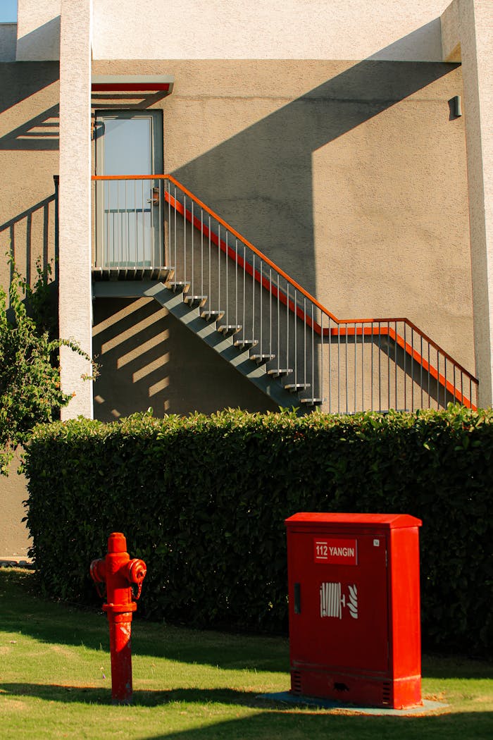 Red fire hydrant and box beside a modern staircase outdoors in sunlight.